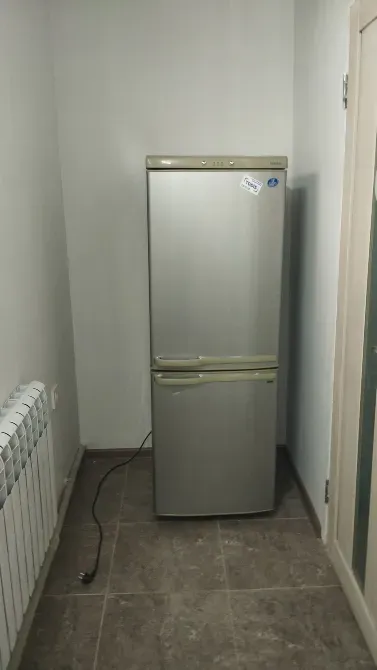 Серебристый холодильник в углу комнаты на фоне плитки