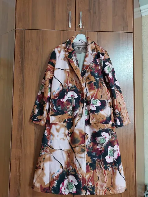 Пуховик с цветочным принтом, висит на вешалке в помещении с деревянными стенами