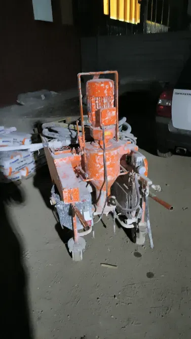 Оранжевый строительный аппарат на фоне грязного пола и автомобиля