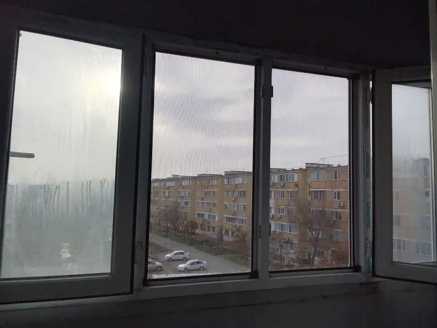 Вид из окна с запотевшими стеклами на жилые здания и улицу