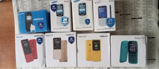 Коробки мобильных телефонов Nokia и Samsung на столе, среди которых модели Nokia 110 и Samsung SM-B310E