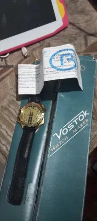 Часы Vostok с золотым циферблатом и черным ремешком, упакованные в коробку с инструкцией