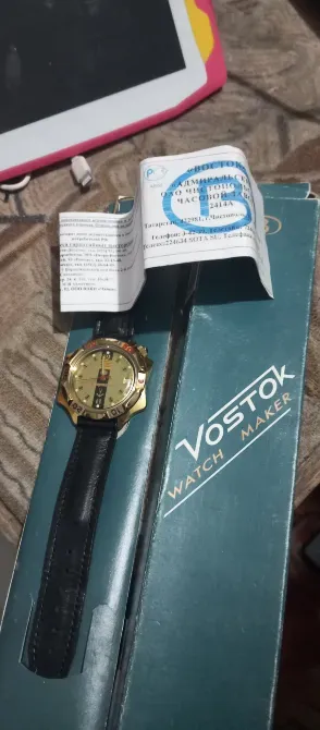 Часы Vostok с золотым циферблатом и черным ремешком, упакованные в коробку с инструкцией