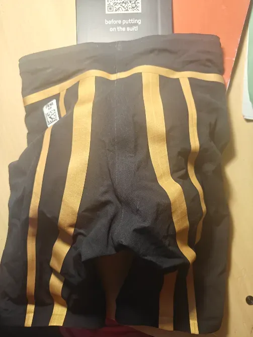 Потертые купальные шорты с черными и золотыми полосами, лежащие на столе рядом с QR-кодом