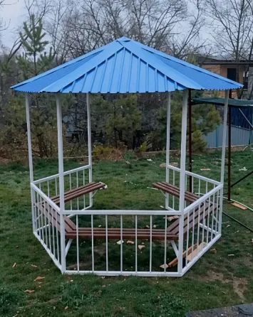 Беседка с синей крышей и белым каркасом на зеленом травяном участке