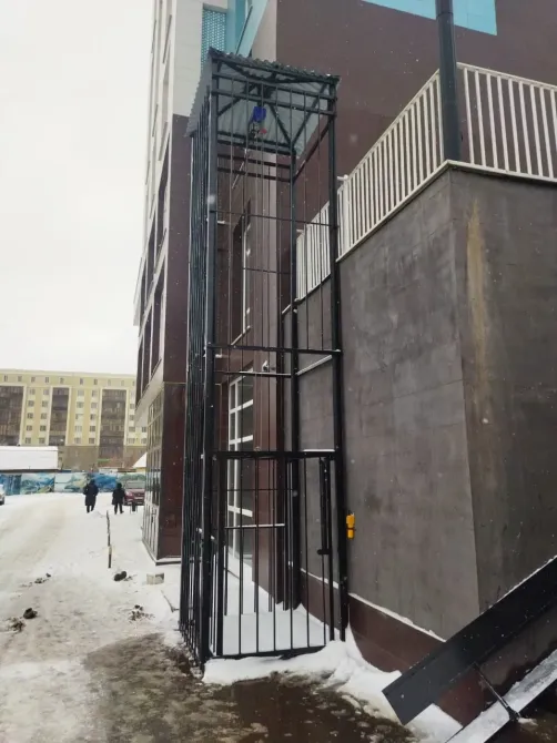 Вертикальный подъемник с защитной решеткой у современного здания в зимних условиях