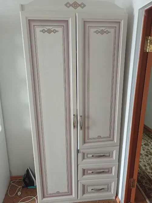 Шкаф с двумя дверцами и тремя выдвижными ящиками, оформленный в светлых тонах с декоративными элементами