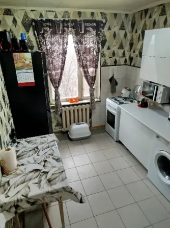 Кухня с белыми кухонными шкафами, плитой и стиральной машиной, окнами с занавесками в геометрический узор