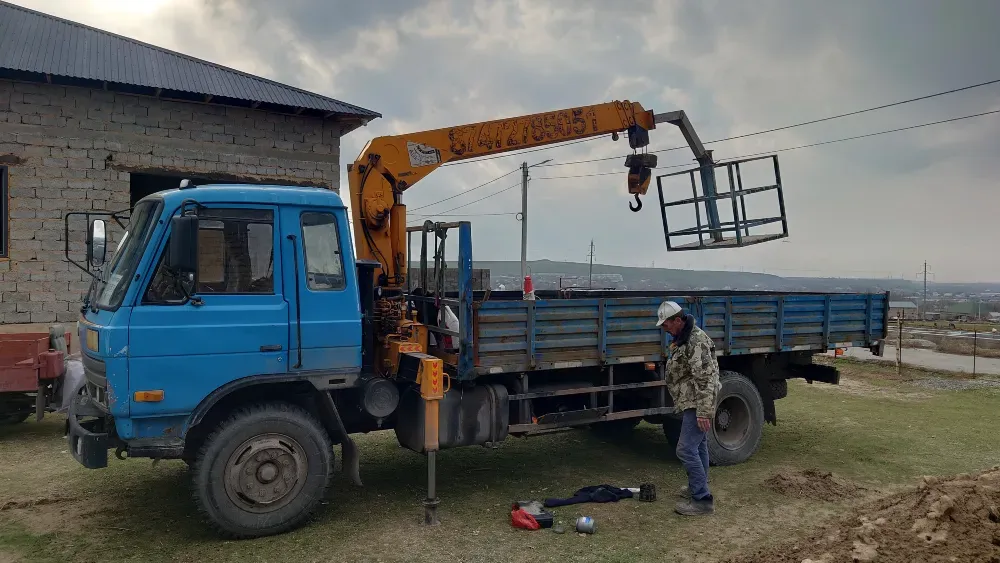 Грузовик с краном, работник рядом с кузовом в процессе установки оборудования