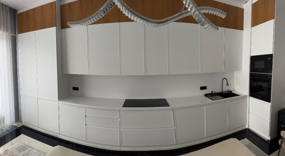 Современная кухня с белыми и деревянными шкафами, встроенной техникой и черной столешницей