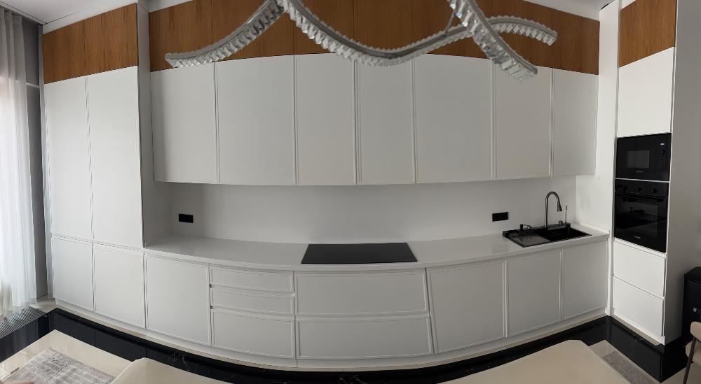 Современная кухня с белыми и деревянными шкафами, встроенной техникой и черной столешницей