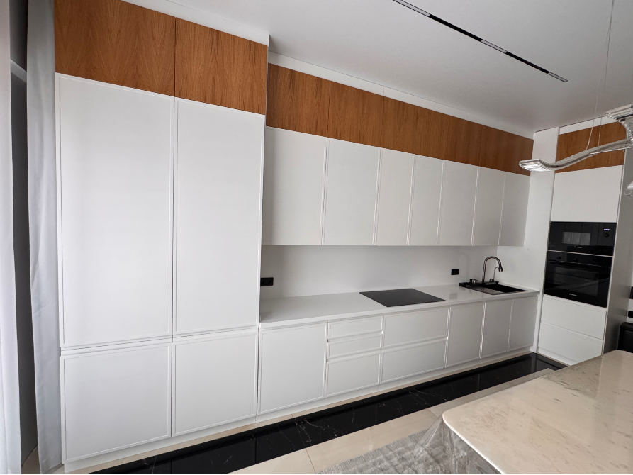 Кухня с белыми фасадами, элементами из дерева, встроенной плитой и раковиной