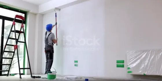 Рабочий, заливающий стену краской в комнате