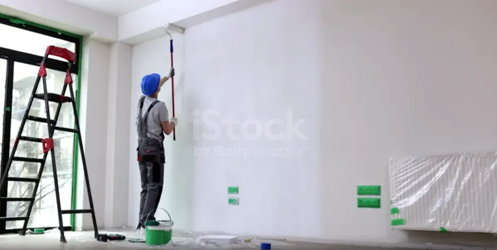 Рабочий, заливающий стену краской в комнате