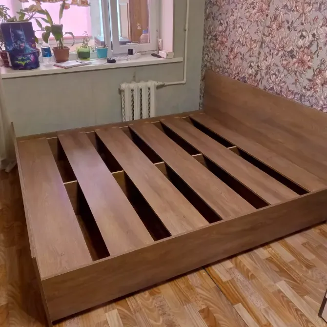 Двуспальная кровать с проложенными лагами и стильным внешним видом, установленная в интерьере с цветами на подоконнике