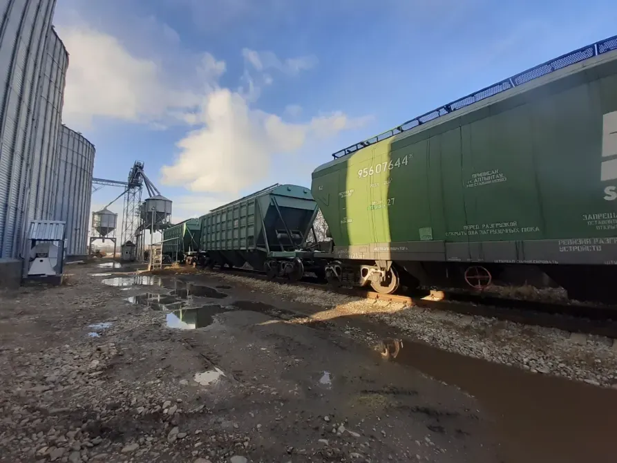 грузовые поезда на железнодорожной станции с цистернами и силосами на фоне неба с облаками