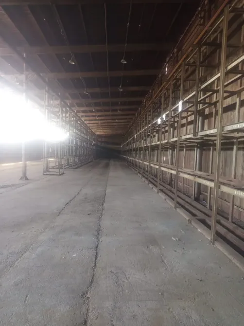 Узкий проход между металлическими стеллажами в длинном складе