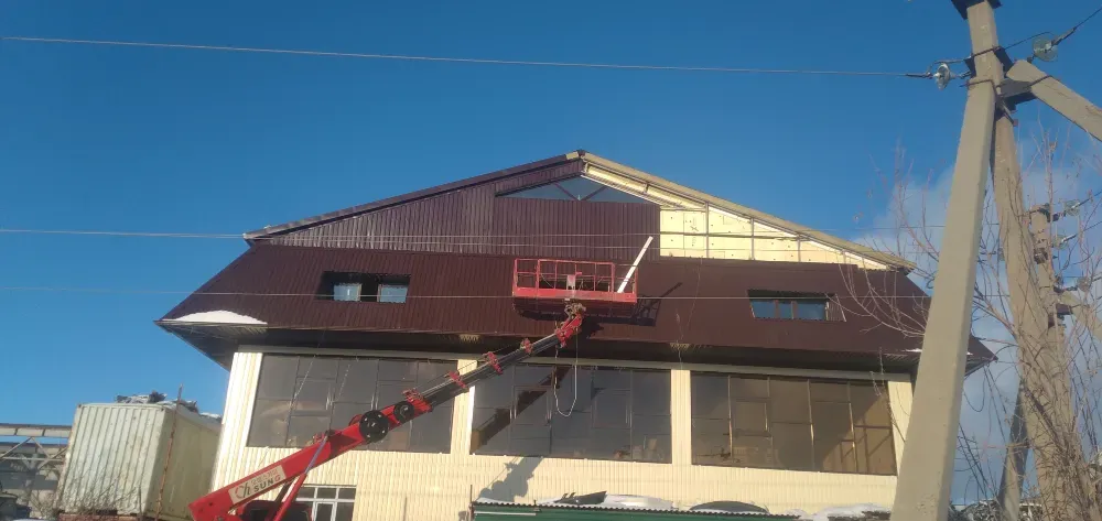 Работа по ремонту крыши здания с использованием подъемника на фоне голубого неба