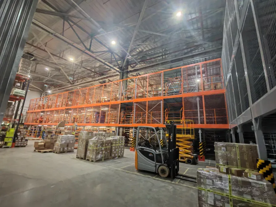 Современное складское помещение с высокими стеллажами и штабелером среди упаковок