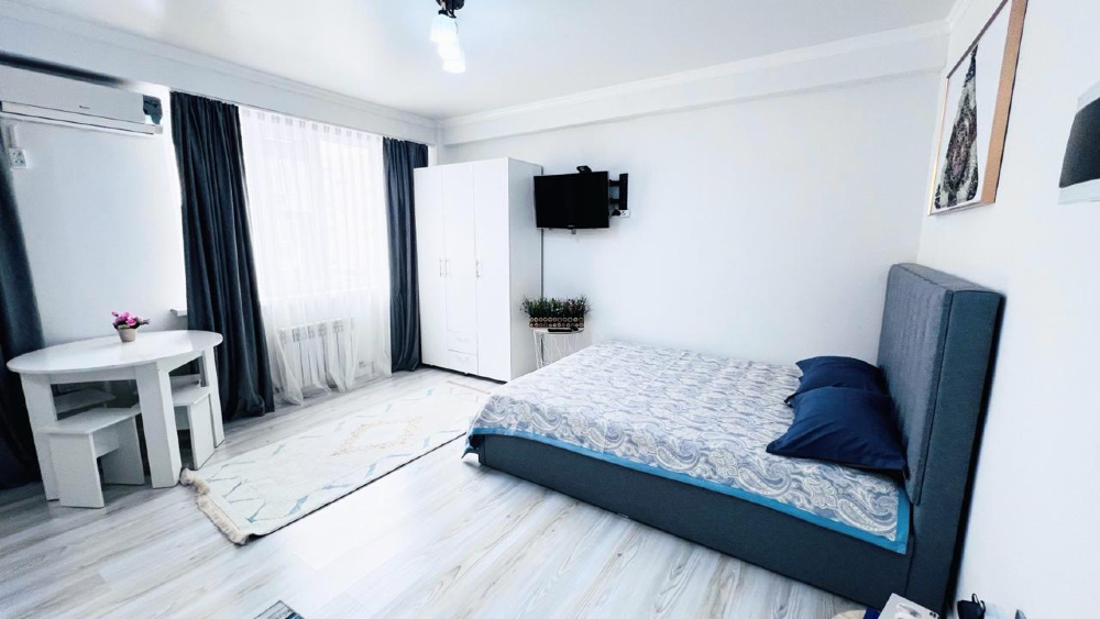 Современный интерьер комнаты с двуспальной кроватью, телевизором и обеденной зоной