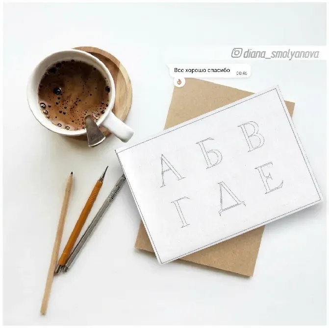 Чашка кофе на деревянной подставке, карандаши и лист бумаги с буквами русского алфавита