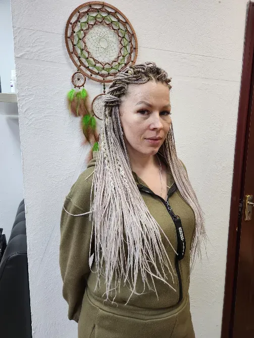 Женщина с длинными косами в нейтральных тонах, стоящая на фоне украшенного стенда