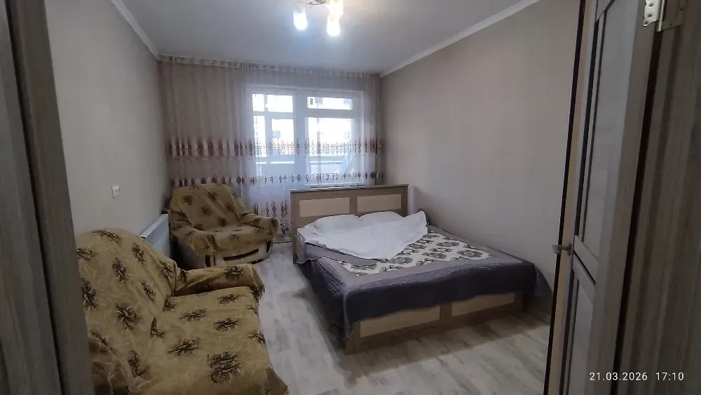 Спальня с одной двуспальной кроватью и диваном, оформленная в нейтральных тонах