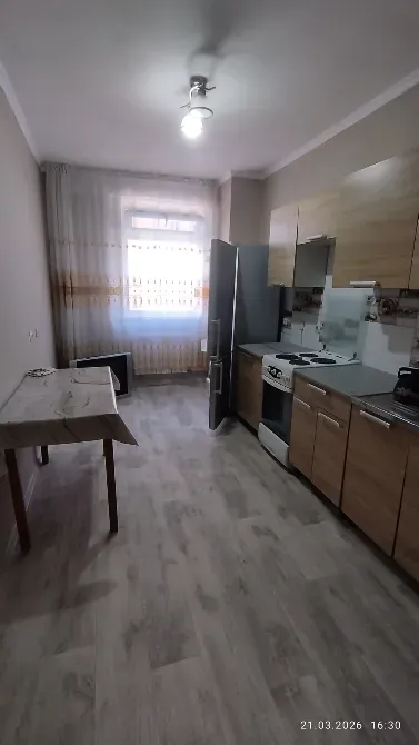 Кухня с столом, холодильником и плитой, оформленная в светлых тонах