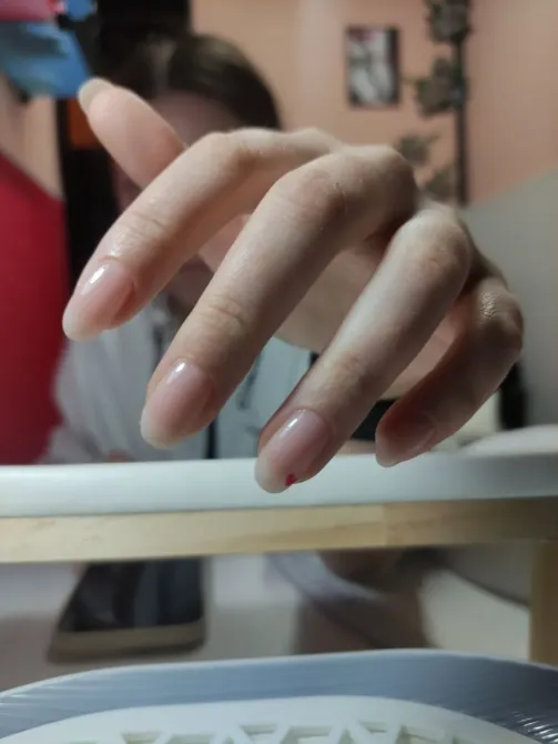 Рука с незаконченной процедурой маникюра на фоне рабочего стола