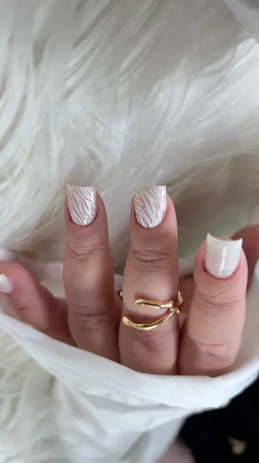 Рука с белым маникюром и золотым кольцом на фоне пушистой ткани