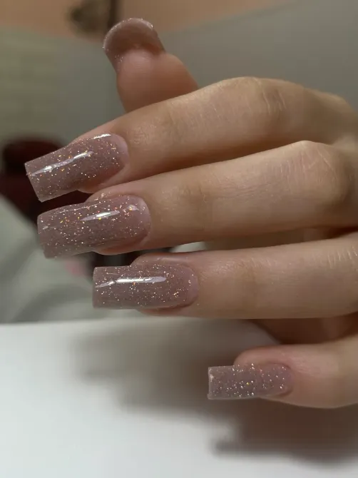 Рука с длинными ногтями, украшенными блестками, на фоне светлого стола