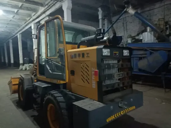 Экскаватор-погрузчик в складском помещении с желтой ковшовой лопатой