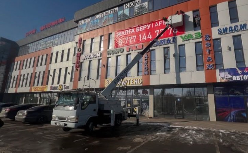 Грузовой автомобиль с подъемной установкой, устанавливающий рекламу на здании