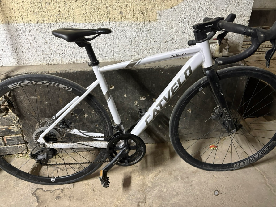 Байк марки FATVELD, белого цвета, с состоящимися колесами и велосипедом на фоне стены