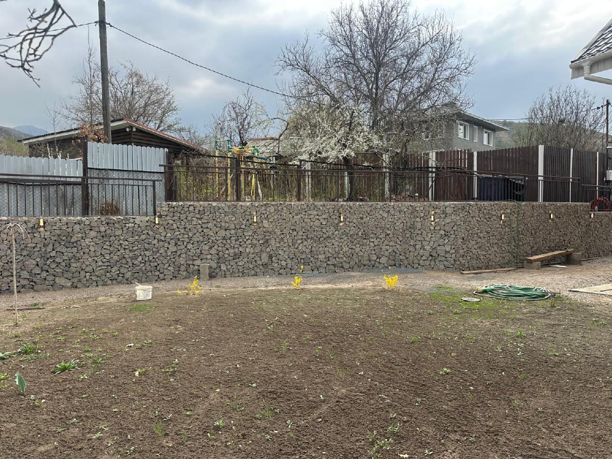 Габионовая стена с зелеными растениями на фоне дома