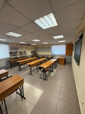 Бос сынып, ағаш үстелдер мен орындықтармен, төбелік шамдармен жарықтандырылған, перделермен жабылған үлкен терезелер, оқыту материалдарымен безендіріл