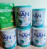 Nestlé NAN және Nestogen сүт қоспалары, әр түрлі жастағы сәбилерге арналған, ақ фонның үстінде.