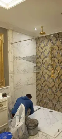Рабочий укладывает плитку в ванной комнате с мраморной отделкой и декоративной стеной