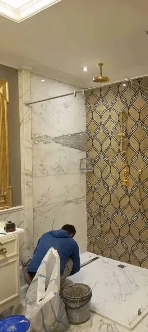 Рабочий укладывает плитку в ванной комнате с мраморной отделкой и декоративной стеной