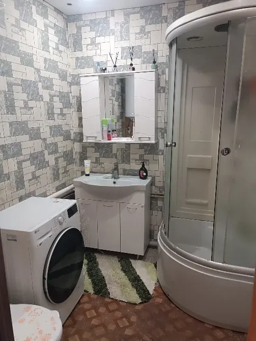 Ванная комната с стиральной машиной, душевой кабиной и зеркалом, оформленная в светлых тонах