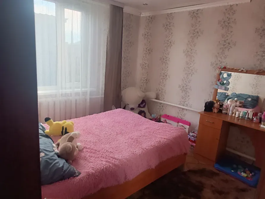 Спальня с розовым покрывалом на кровати, зеркалом и игрушками на тумбочке