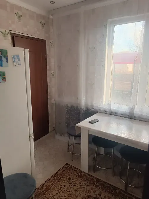 Уютное пространство с обеденным столом и стульями, кухня с холодильником и окном