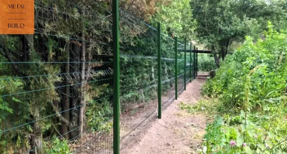 Забор из металлической сетки на проселочной дороге между деревьями