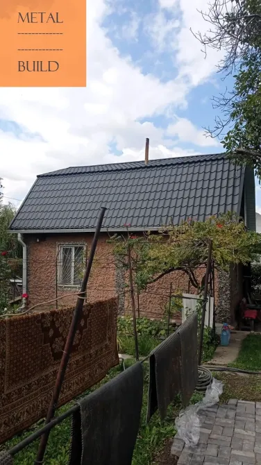 Дом с черной крышей и зелеными насаждениями вокруг