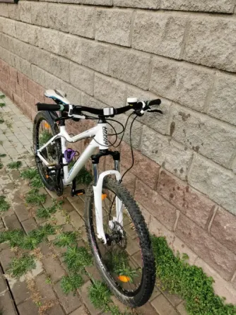 Белый горный велосипед с черными и синими деталями, стоящий на плитке рядом со стеной