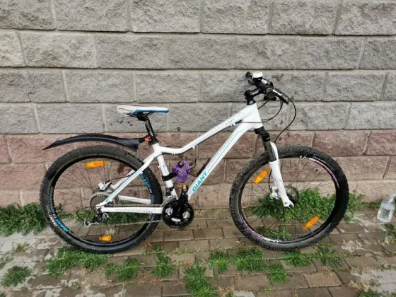 Белый горный велосипед с черными и синими деталями, стоящий на плитке рядом со стеной