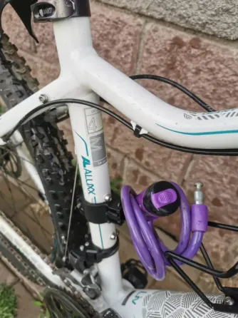 Белый горный велосипед с черными и синими деталями, стоящий на плитке рядом со стеной