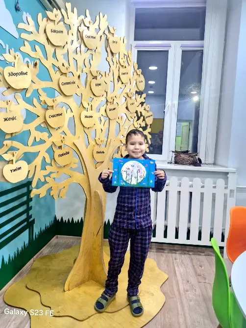 Мальчик с рисунком на фоне дерева, украшенного символами