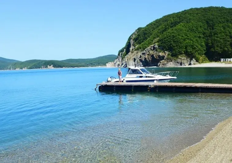 Пляжный пейзаж с пирсом и лодкой на фоне зеленых холмов