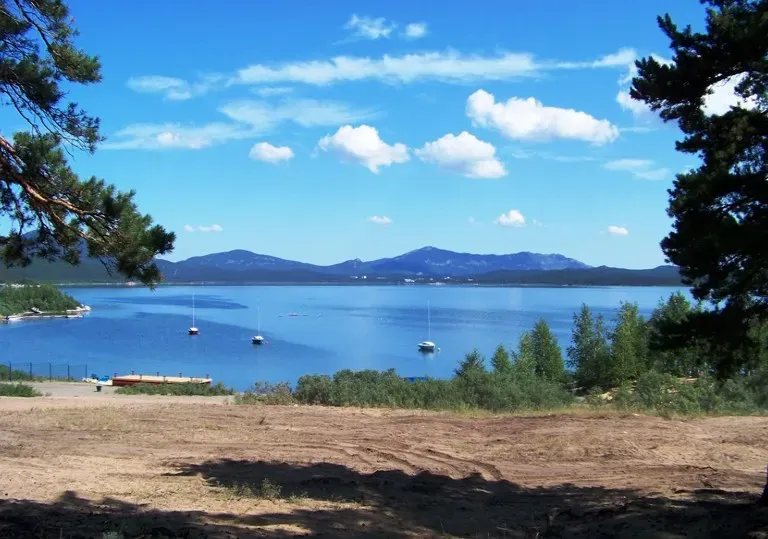 Вид на водоем с лодками на фоне гор и облаков